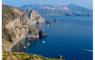 Stunning view of Valle Muria beach in Lipari and the Faraglioni. In the background the crater of Vulcano Island. 
